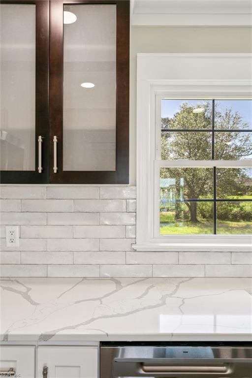 room details with light stone counters, tasteful backsplash, stainless steel dishwasher, and white cabinets