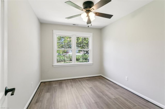 empty room with baseboards, ceiling fan, wood finished floors, and visible vents