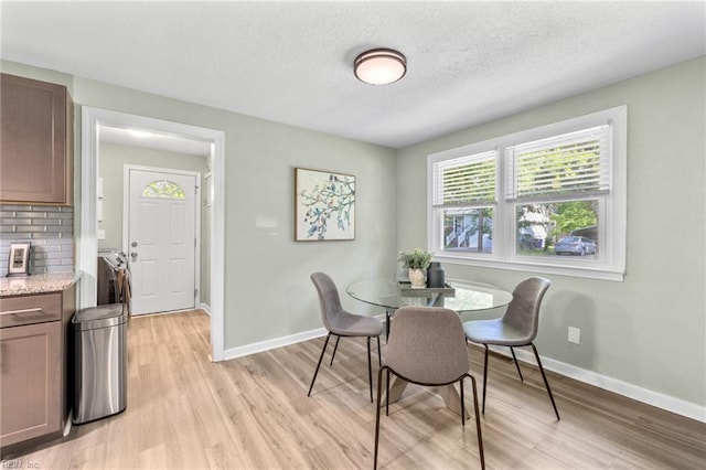 dining room featuring baseboards, a textured ceiling, and light wood-style floors