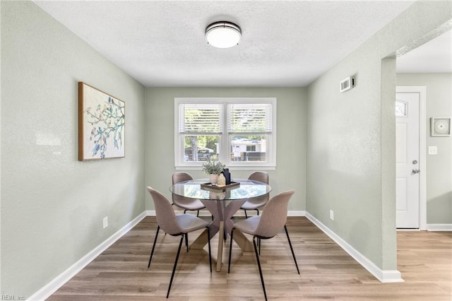 dining space featuring a textured ceiling, a textured wall, baseboards, and light wood-type flooring