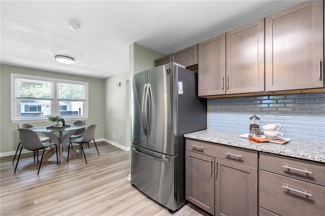 kitchen featuring freestanding refrigerator, backsplash, baseboards, and light wood finished floors