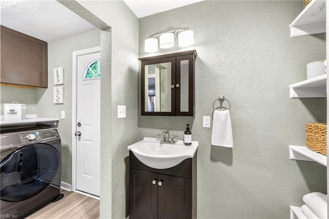 bathroom with a textured wall, washer / dryer, wood finished floors, and vanity