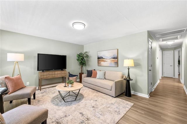 living area featuring light wood-style floors, baseboards, a textured ceiling, and visible vents