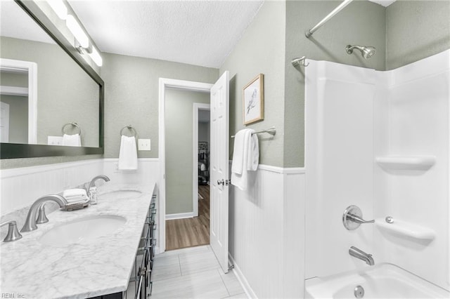 bathroom featuring a sink, a wainscoted wall, a textured ceiling, and shower / washtub combination