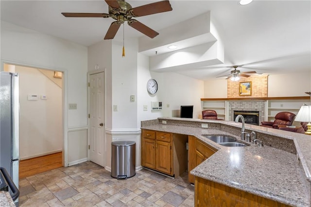 kitchen with a sink, freestanding refrigerator, a ceiling fan, open floor plan, and stone tile flooring