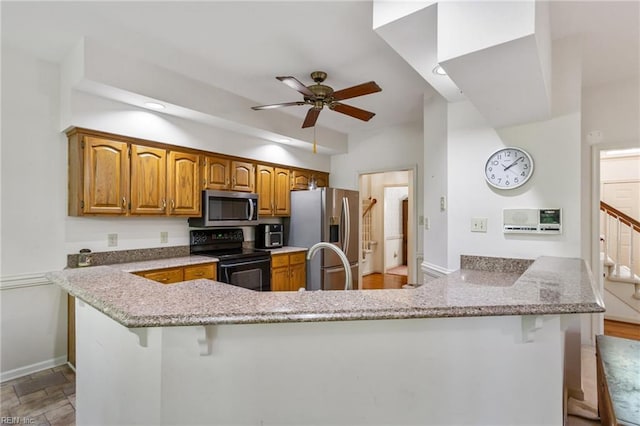 kitchen featuring a ceiling fan, brown cabinets, a kitchen bar, and stainless steel appliances