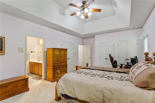 bedroom featuring two closets, ensuite bathroom, ceiling fan, light colored carpet, and a tray ceiling