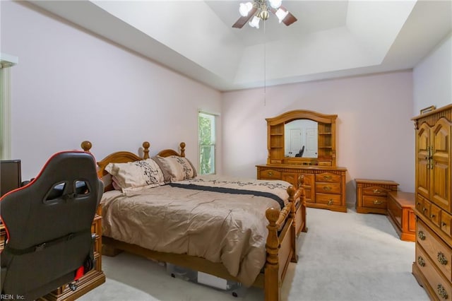 bedroom with a raised ceiling, ceiling fan, and light colored carpet