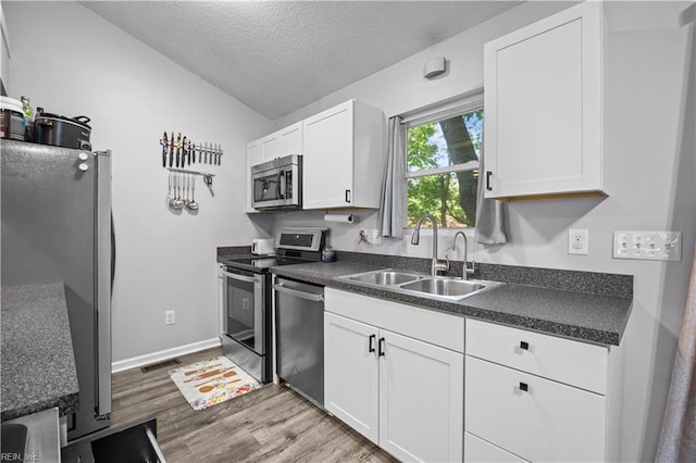 kitchen featuring dark countertops, light wood-type flooring, a textured ceiling, a sink, and appliances with stainless steel finishes