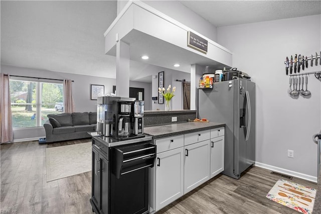 kitchen featuring dark wood-style flooring, dark countertops, stainless steel fridge, and white cabinetry