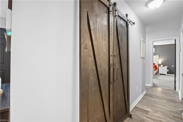 corridor featuring baseboards, a textured ceiling, a barn door, and wood finished floors