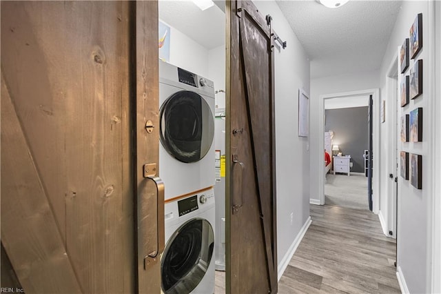 laundry area featuring laundry area, a barn door, baseboards, light wood-style floors, and stacked washer and clothes dryer