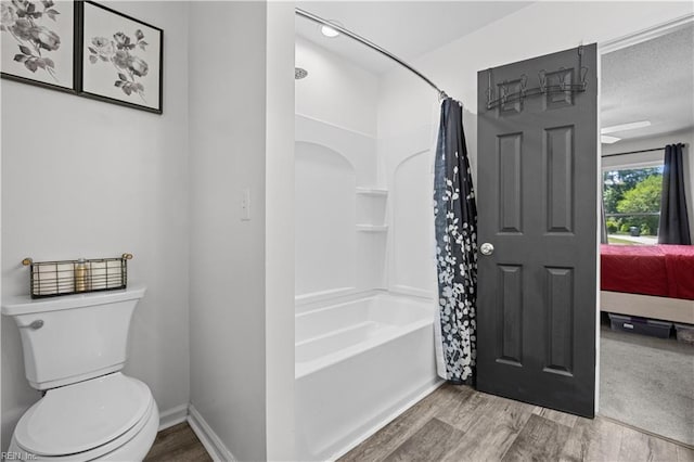 ensuite bathroom featuring shower / tub combo with curtain, wood finished floors, toilet, baseboards, and connected bathroom