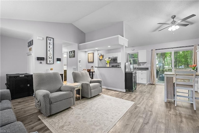 living area with ceiling fan, visible vents, lofted ceiling, and light wood-style floors