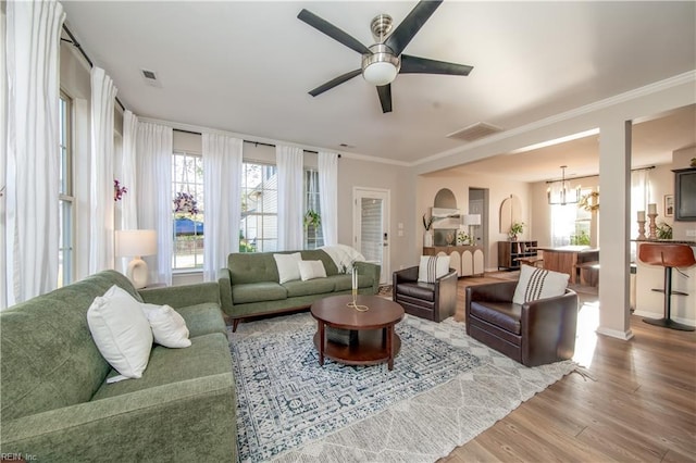 living area featuring a healthy amount of sunlight, ceiling fan with notable chandelier, wood finished floors, and visible vents
