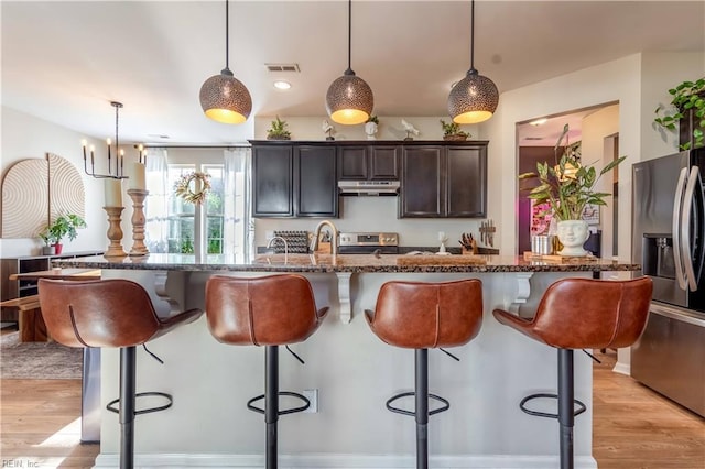 kitchen featuring visible vents, a kitchen breakfast bar, under cabinet range hood, dark stone countertops, and appliances with stainless steel finishes