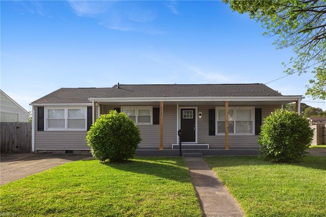 view of front facade featuring a porch, roof with shingles, fence, and a front yard