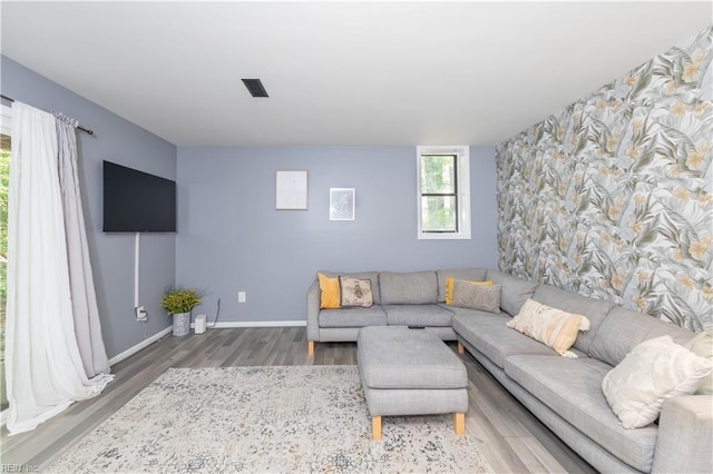 living area featuring baseboards, an accent wall, wood finished floors, and visible vents