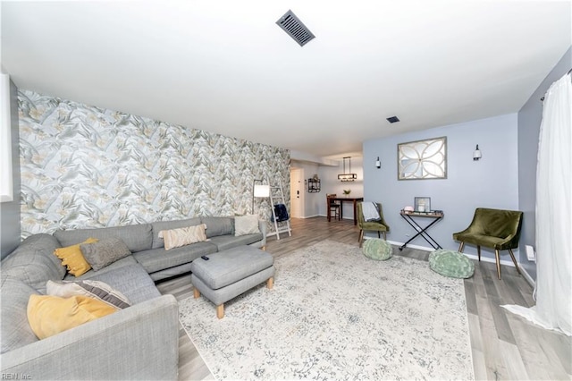 living area featuring visible vents, wood finished floors, an accent wall, baseboards, and wallpapered walls