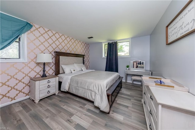 bedroom with wood finished floors, baseboards, an accent wall, and wallpapered walls