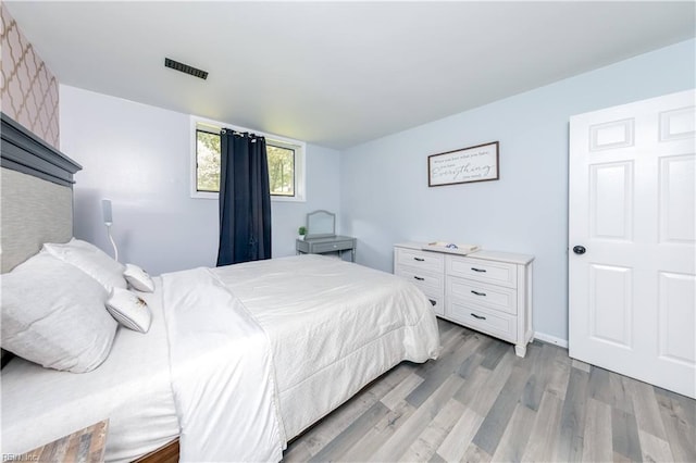 bedroom with baseboards, light wood finished floors, and visible vents