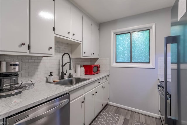 kitchen featuring stainless steel dishwasher, light countertops, white cabinets, tasteful backsplash, and a sink