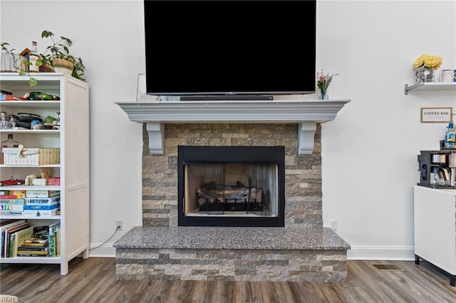 interior details with a fireplace with raised hearth, baseboards, visible vents, and wood finished floors