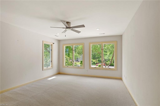 carpeted empty room featuring plenty of natural light, a ceiling fan, baseboards, and visible vents