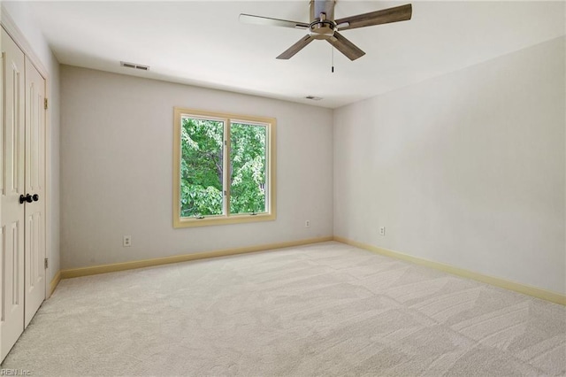 spare room with baseboards, ceiling fan, light colored carpet, and visible vents