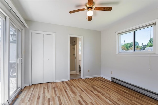 unfurnished bedroom with multiple windows, a baseboard heating unit, and light wood-style flooring