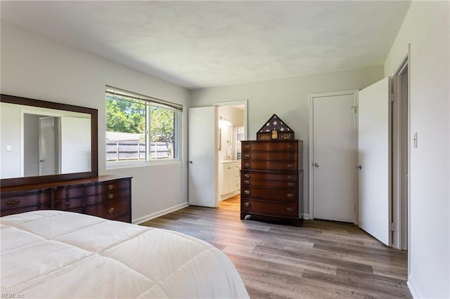 bedroom featuring baseboards, wood finished floors, and ensuite bath