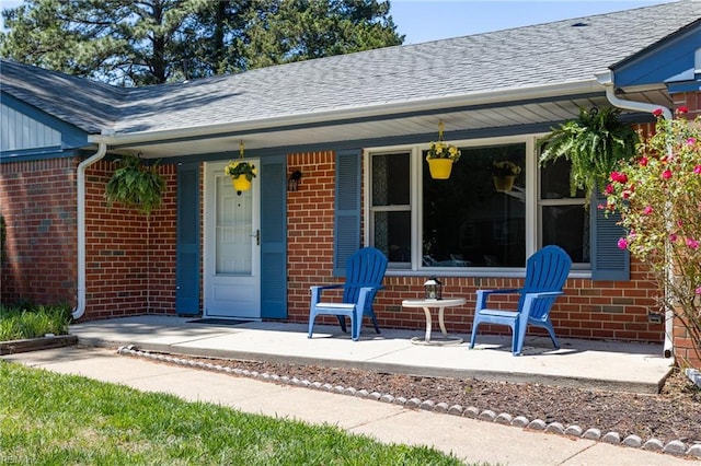 doorway to property featuring brick siding, a shingled roof, and covered porch