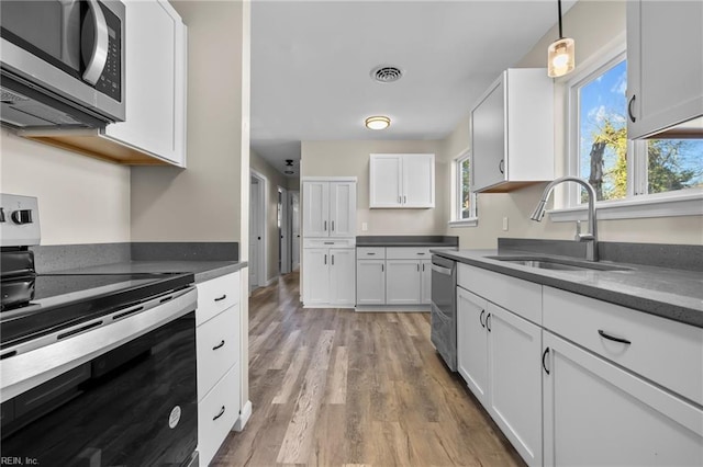 kitchen featuring dark countertops, white cabinets, a sink, light wood-style flooring, and appliances with stainless steel finishes