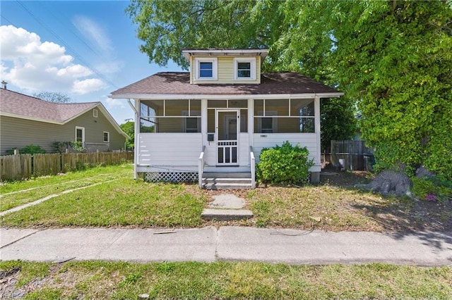 bungalow with fence, a shingled roof, a sunroom, and a front yard