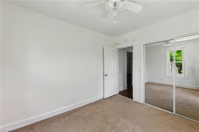 unfurnished bedroom featuring ceiling fan, a textured ceiling, a closet, ornamental molding, and carpet
