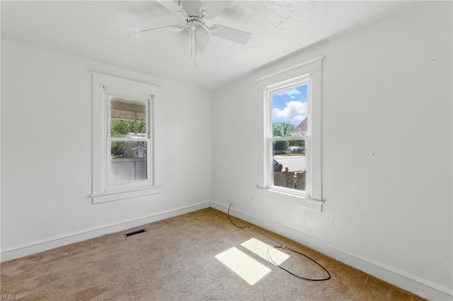 carpeted empty room with a healthy amount of sunlight, baseboards, ceiling fan, and visible vents