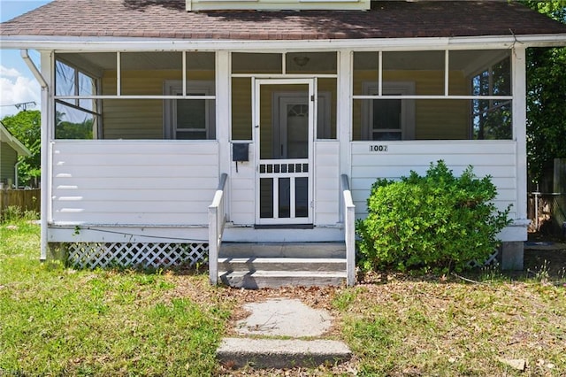 entrance to property featuring a shingled roof and a yard