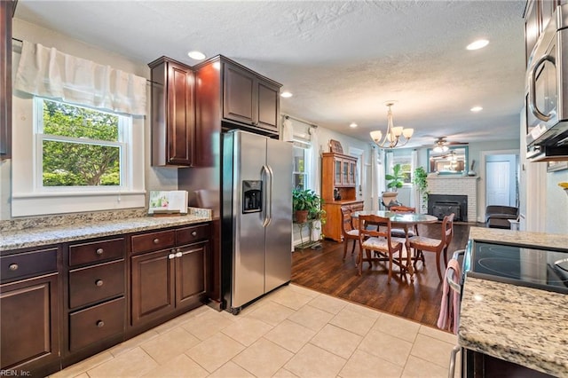 kitchen featuring a brick fireplace, light tile patterned floors, stainless steel appliances, and a healthy amount of sunlight