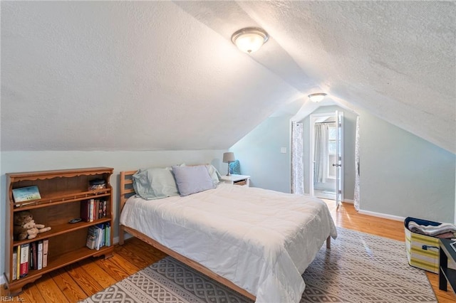 bedroom with a textured ceiling, wood finished floors, and lofted ceiling