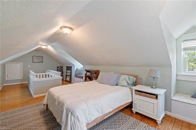 bedroom featuring lofted ceiling, a textured ceiling, baseboards, and wood finished floors