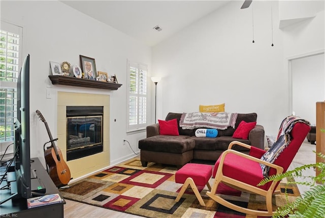 living area with a ceiling fan, visible vents, a fireplace, wood finished floors, and high vaulted ceiling