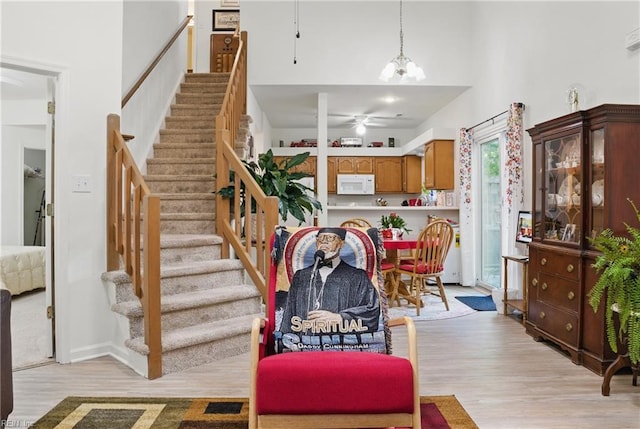staircase with a high ceiling, ceiling fan with notable chandelier, and wood finished floors