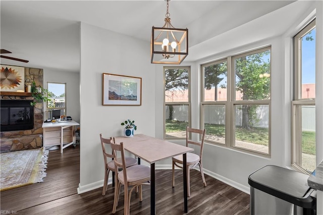 dining room featuring baseboards, dark wood-style flooring, a stone fireplace, and a notable chandelier
