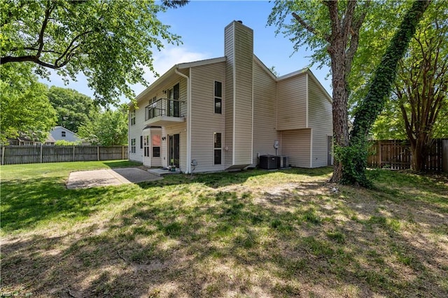 rear view of property with a balcony, a patio, a fenced backyard, a chimney, and a yard