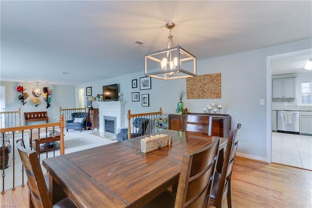 dining room with an inviting chandelier, light wood finished floors, a glass covered fireplace, baseboards, and visible vents