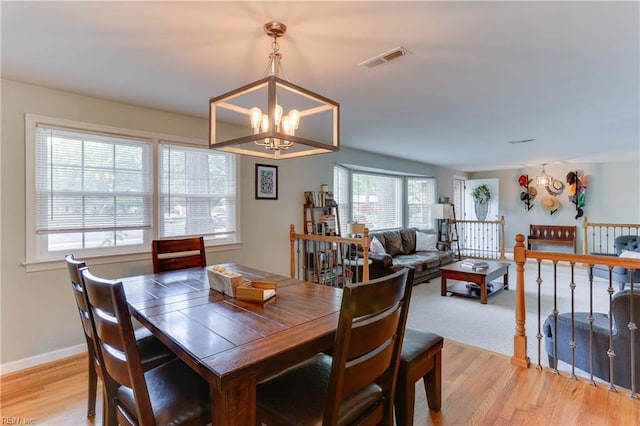 dining area with baseboards, a notable chandelier, light wood-style flooring, and visible vents