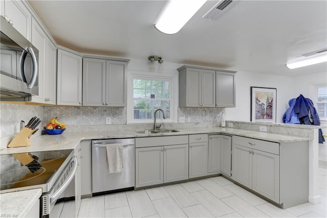 kitchen featuring visible vents, a peninsula, gray cabinets, a sink, and stainless steel appliances