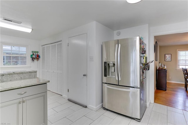 kitchen with visible vents, baseboards, stainless steel fridge, light stone counters, and light tile patterned floors