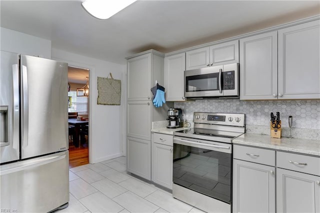 kitchen with gray cabinets, appliances with stainless steel finishes, tasteful backsplash, light tile patterned floors, and light stone counters