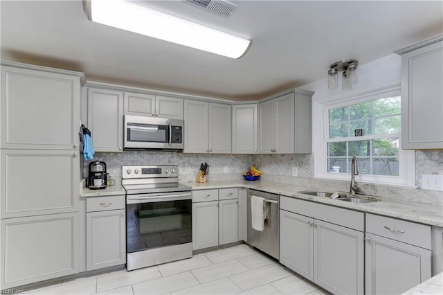 kitchen featuring gray cabinets, decorative backsplash, visible vents, appliances with stainless steel finishes, and a sink